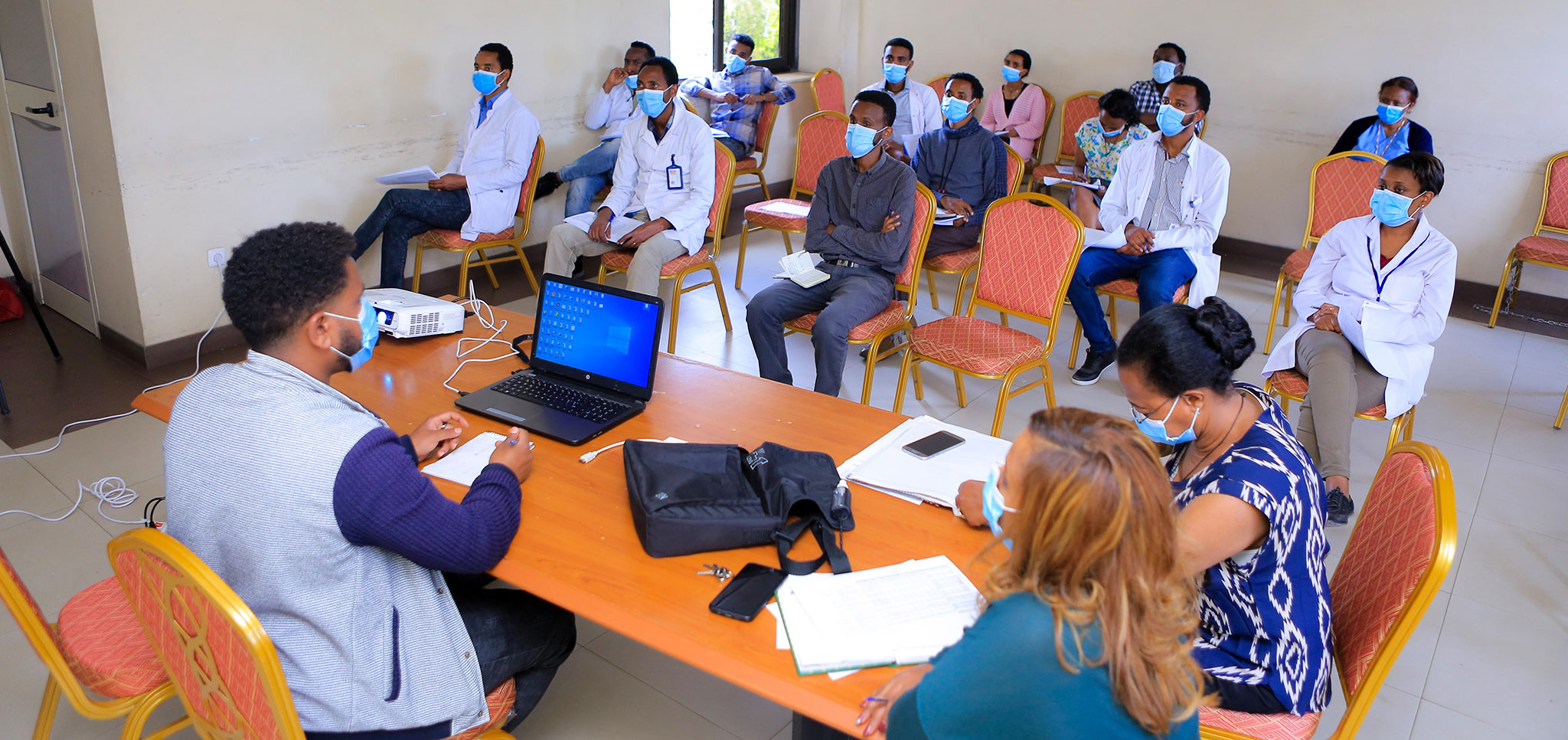 Photo of several people in white coats and medical masks attending a meeting