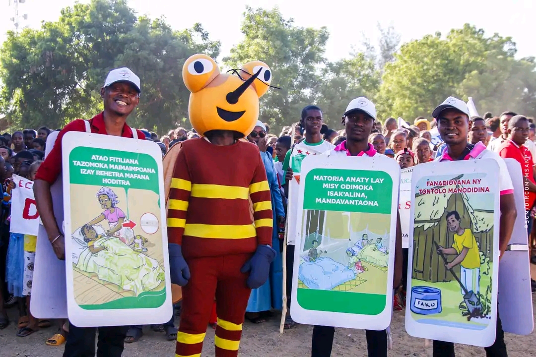 Three people holding signs featuring malaria messaging and one person wears mosquito costume