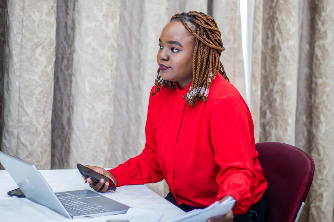 Photograph of a woman holding a smartphone with a laptop