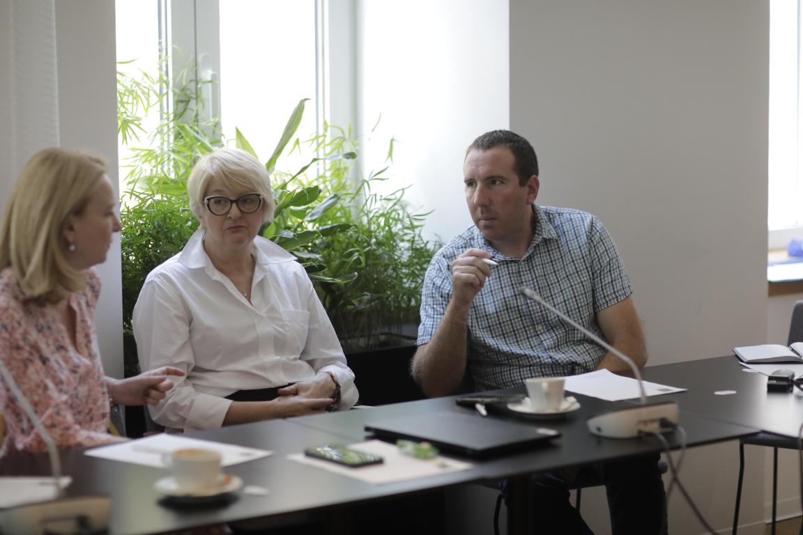 A man sits at a table and speaks with two women seated beside him.