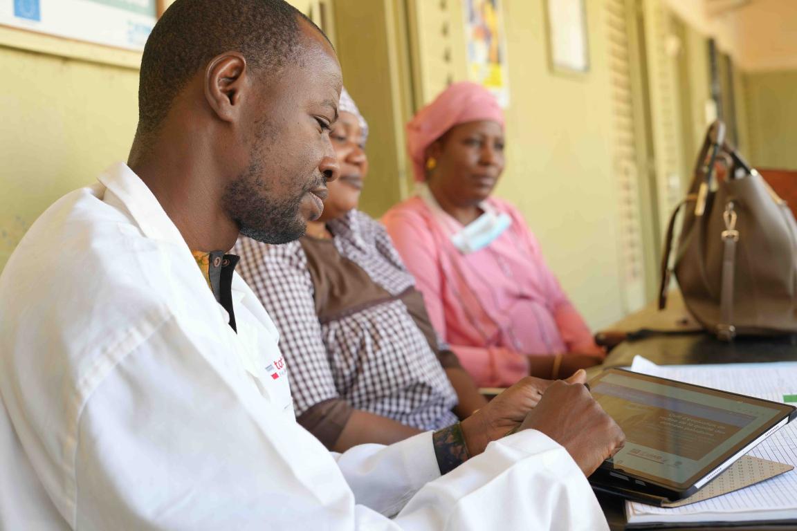 A man in a white coat works on his tablet with his team members sitting beside him